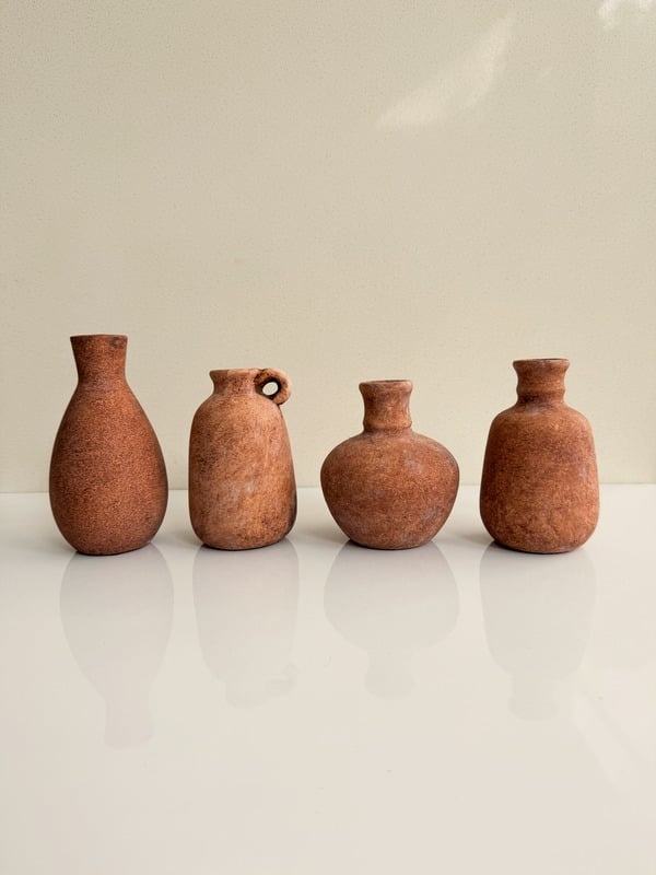 Cuatro jarrones pequeños de terracota, de formas distintas, sobre una superficie clara.