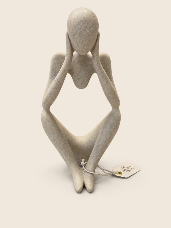 Figura de cerámica blanca de una persona sentada, pensativa, con las manos en la cabeza.