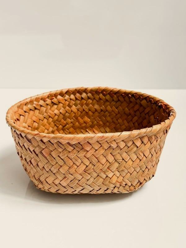 Canasta redonda de hoja de palma tejida a mano, sobre una superficie clara con luz natural.